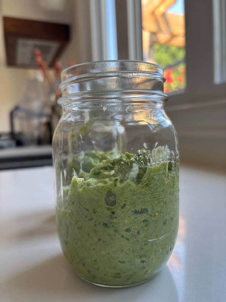 Green garlic scape pesto in a jar on a white counter with a window in the background.